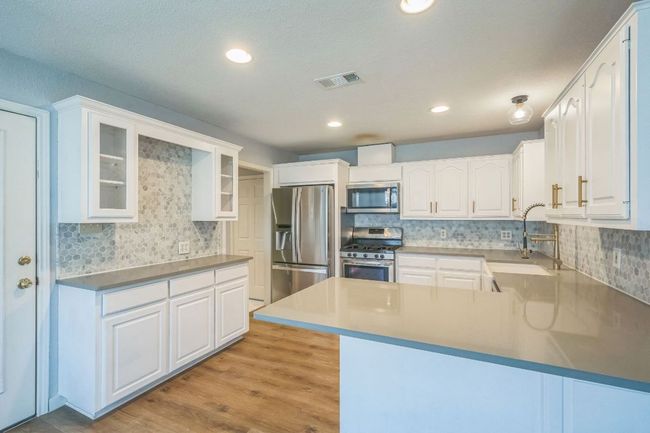 Kitchen featuring appliances with stainless steel finishes, decorative backsplash, glass insert cabinets, white cabinets, and light wood-type flooring | Image 9