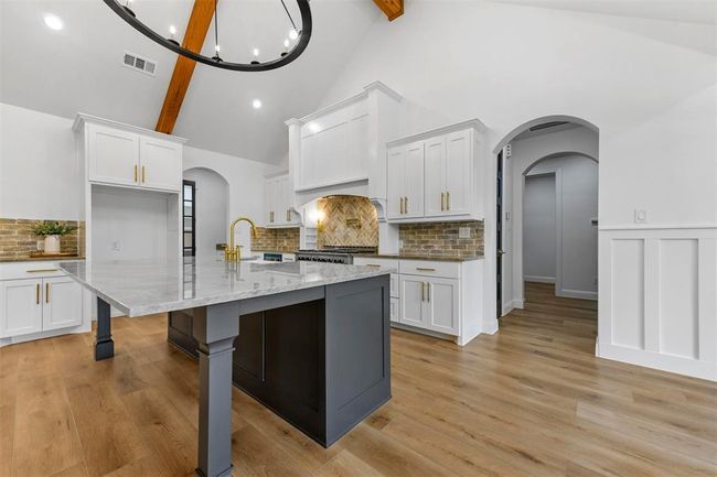 Kitchen featuring white cabinets, beamed ceiling, light stone countertops, light wood-type flooring, and tasteful backsplash | Image 12