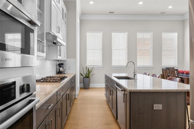 Kitchen with appliances with stainless steel finishes, crown molding, white cabinetry, a center island with sink, and light wood-type flooring | Image 9