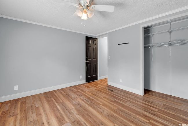 Unfurnished bedroom with a textured ceiling, wood finished floors, a closet, ornamental molding, and baseboards | Image 26