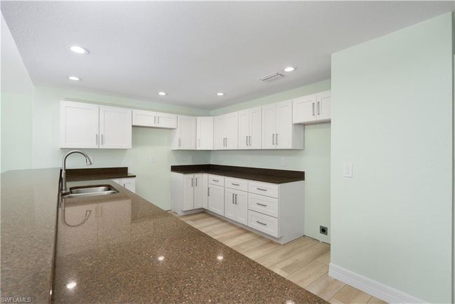 Kitchen featuring dark stone countertops, visible vents, white cabinetry, and a sink | Image 7