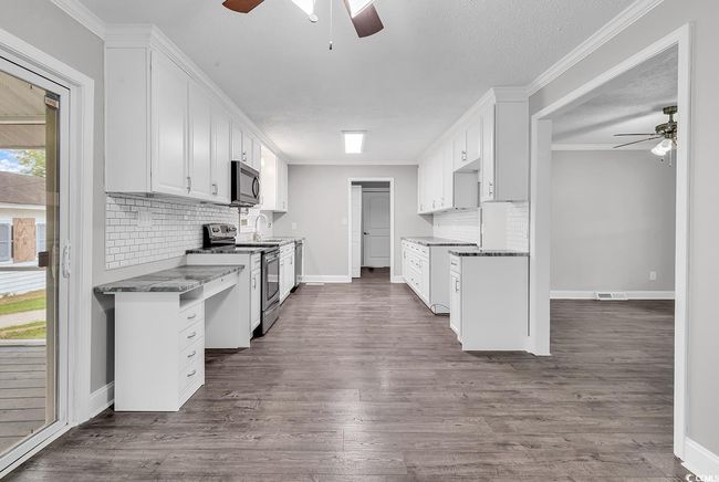 Kitchen featuring a ceiling fan, appliances with stainless steel finishes, backsplash, white cabinets, and ornamental molding | Image 10