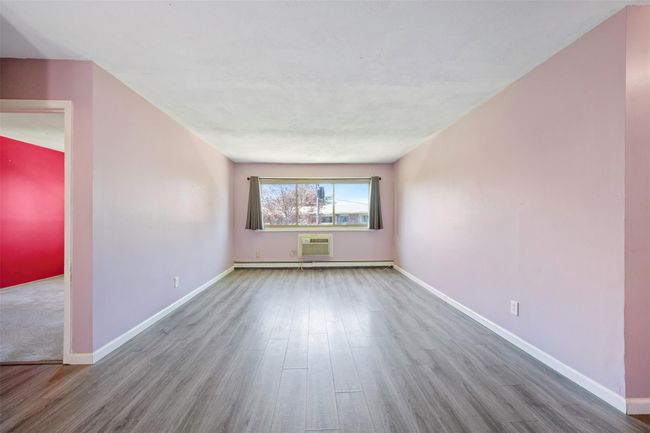Empty room featuring wood finished floors, a baseboard radiator, baseboards, and a wall unit AC | Image 11