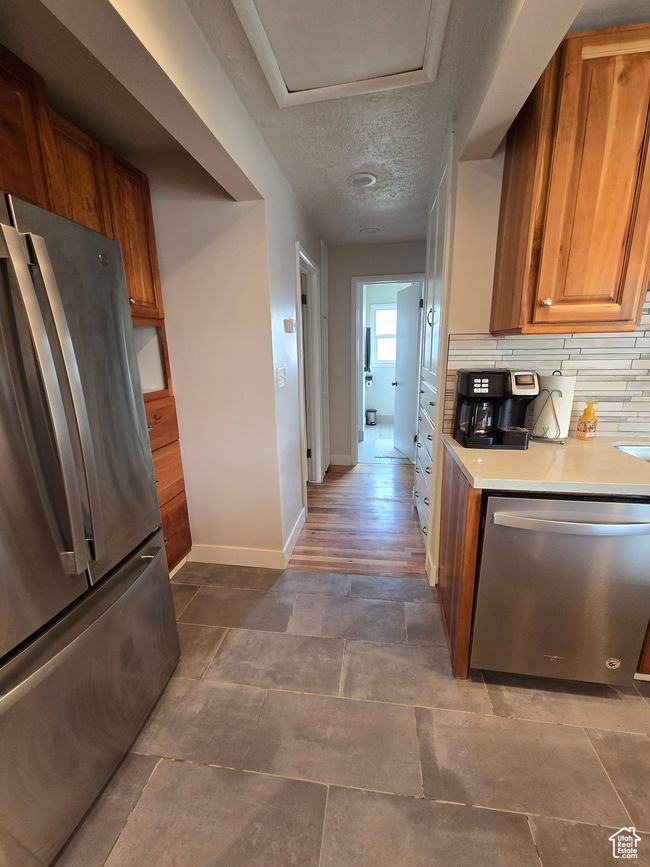 Kitchen with brown cabinets, stainless steel appliances, baseboards, backsplash, and light countertops | Image 20
