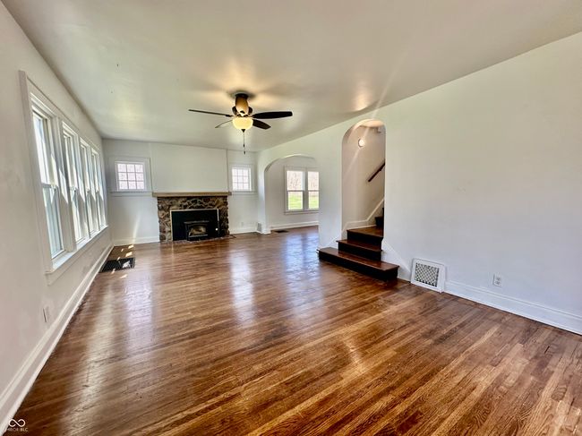 unfurnished living room featuring a fireplace with flush hearth, arched walkways, ceiling fan, and dark wood-style floors | Image 19