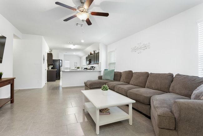 The living room is bright and open with lots of space and opens to the kitchen! It has tall ceilings, a ceiling fan, and tile flooring. | Image 5