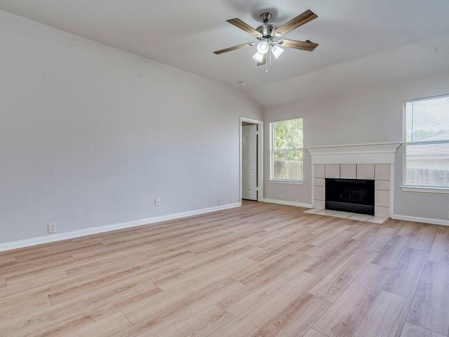 Unfurnished living room featuring light wood-style floors, ceiling fan, lofted ceiling, and a tile fireplace | Image 9