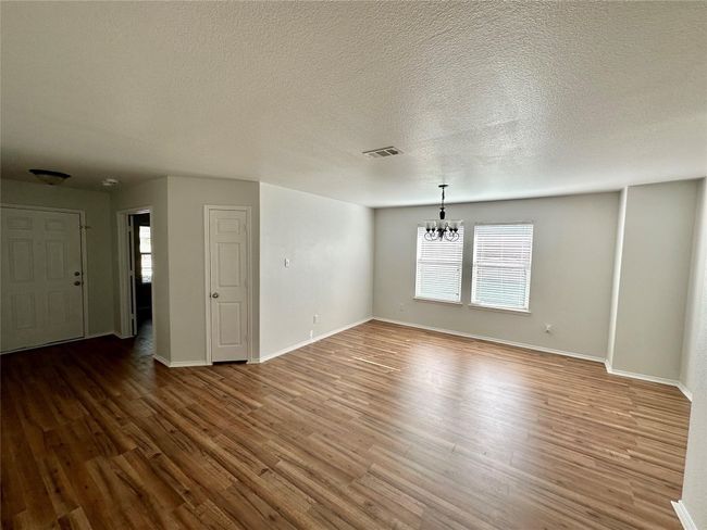 Unfurnished living room featuring baseboards, visible vents, wood finished floors, and a chandelier | Image 6