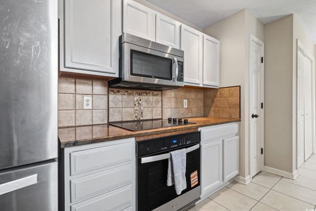 Kitchen with appliances with stainless steel finishes, white cabinets, light tile patterned floors, and backsplash | Image 11