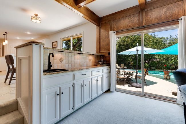 Great room wet bar area with a sink, backsplash, light colored carpet, granite counters, and white cabinets | Image 16