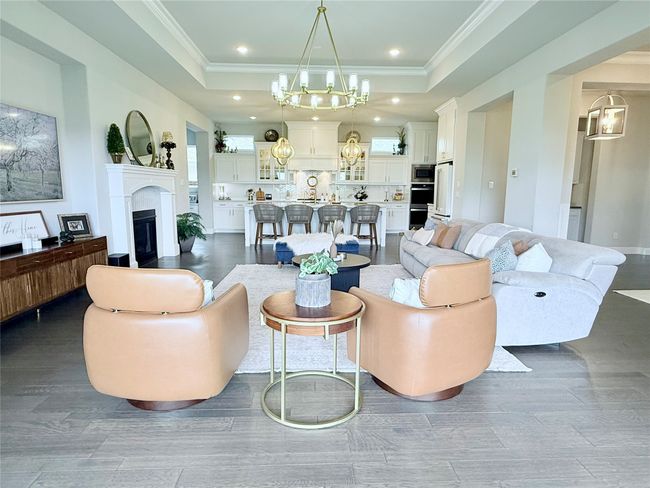 Living room featuring a chandelier, a glass covered fireplace, dark wood-style flooring, recessed lighting, and crown molding | Image 9