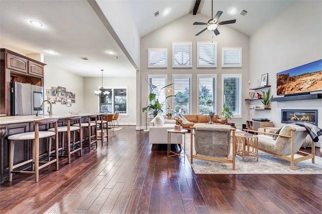 Spacious open-concept living area features prominent ceilings and a wall of windows for abundant natural light with access to the kitchen with a large island and bar seating—perfect for entertaining and everyday living. | Image 12