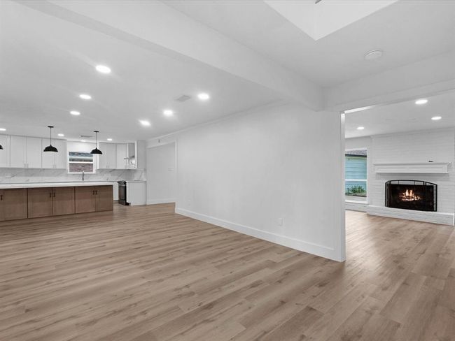 This spacious open-concept area features a modern kitchen with marble countertops, a large island, and pendant lighting. Adjacent is a cozy living room with a fireplace and wood flooring, creating a warm, inviting atmosphere. | Image 5