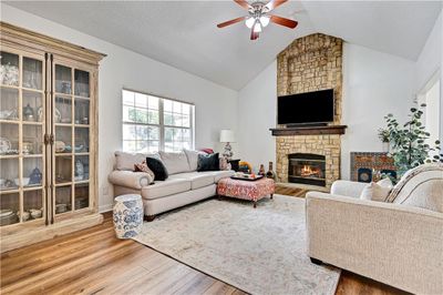 Living room with vaulted ceiling, a stone fireplace, a textured ceiling, ceiling fan, and hardwood / wood-style floors | Image 2