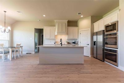 Kitchen with stainless steel appliances, light wood-type flooring, an island with sink, and white cabinets | Image 1