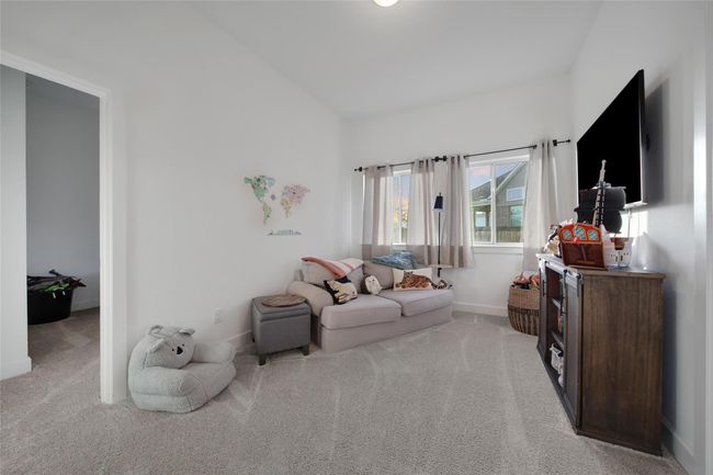 Cozy, carpeted living space with natural light, featuring a comfortable sofa, wall-mounted TV, and decorative accents. Ideal for relaxing or entertaining. | Image 33