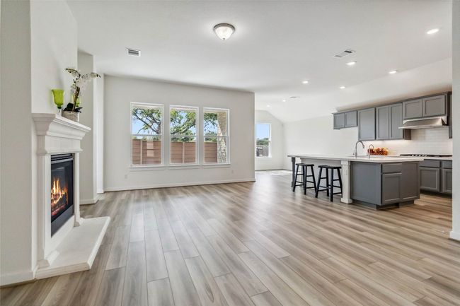 Kitchen with gray cabinets, light wood finished floors, open floor plan, a glass covered fireplace, and vaulted ceiling | Image 5