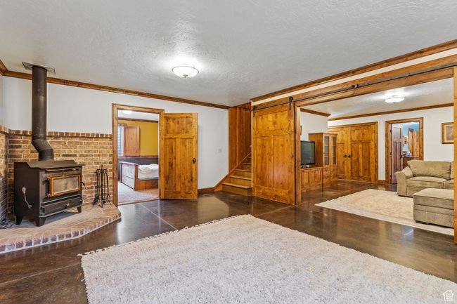 Living room with crown molding, a barn door, a wood stove, and a textured ceiling | Image 32