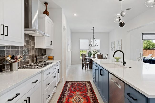 Kitchen featuring backsplash, wall chimney range hood, light countertops, stainless steel appliances, and a sink | Image 10