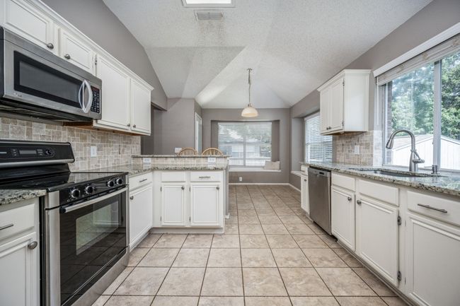 Kitchen with stainless steel appliances, vaulted ceiling, white cabinets, beautiful backsplash, and a peninsula | Image 8
