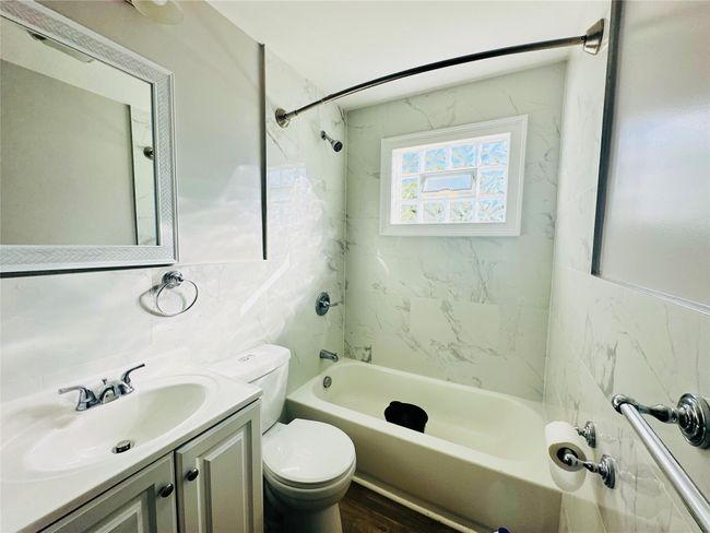 Full bathroom featuring tiled shower / bath combo, hardwood / wood-style floors, toilet, vanity, and tile walls | Image 9