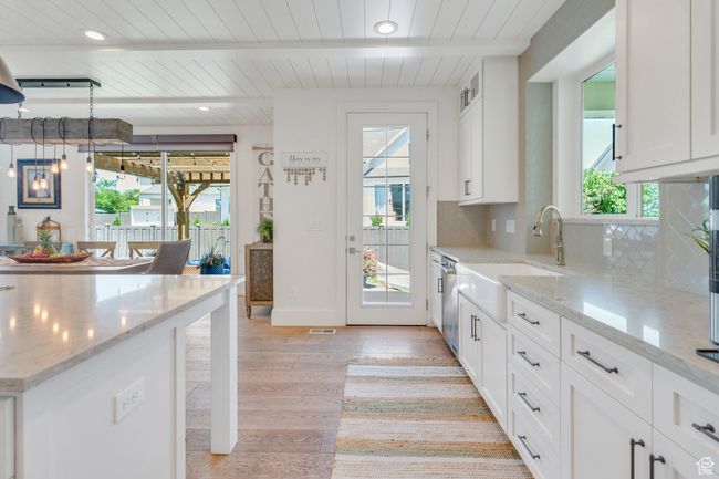 Kitchen featuring light wood-style flooring, tasteful backsplash, a wooden ceiling with exposed beams, white cabinetry, and stainless steel dishwasher | Image 23