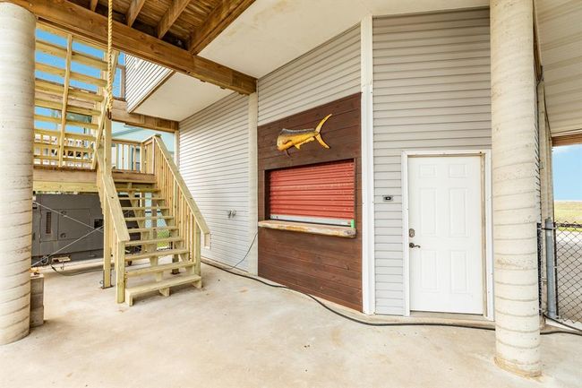 Outdoor bar area under the covered patio. There are recently installed wooden stairs leading to an upper level, a door to an enclosed space, and a decorative fish mounted on the siding. The area has a coastal, rustic charm. | Image 40