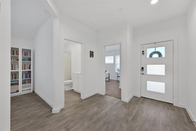 Bright entryway with modern design, featuring wood flooring, a half bath, and access to a cozy carpeted room. Built-in bookshelves offer additional storage. | Image 18