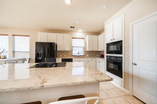 Kitchen featuring black appliances, a kitchen bar, backsplash, light tile patterned floors, and recessed lighting | Image 12