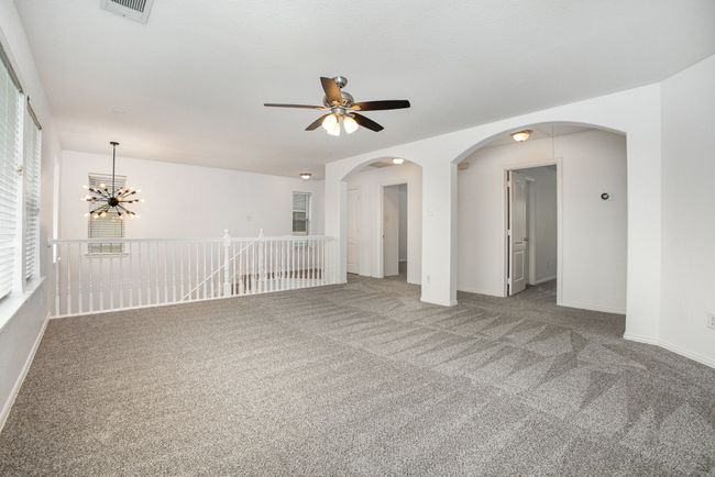 Unfurnished room featuring carpet floors, baseboards, ceiling fan with notable chandelier, and arched walkways | Image 18