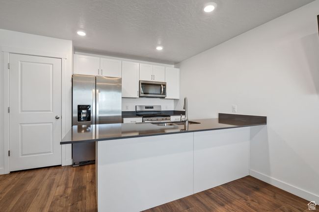 Kitchen featuring dark countertops, a sink, stainless steel appliances, a peninsula, and dark wood-style floors | Image 6
