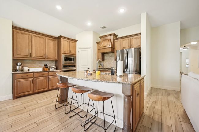 Kitchen featuring custom exhaust hood, arched walkways, appliances with stainless steel finishes, a kitchen bar, and brown cabinets | Image 13