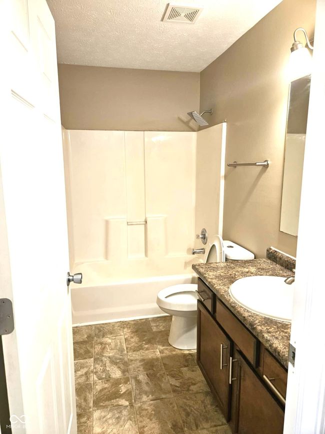 bathroom with a textured ceiling, visible vents, toilet, shower / bath combination, and vanity | Image 37