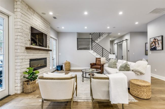 Living area featuring a barn door, a fireplace, wood finished floors, stairs, and baseboards | Image 15