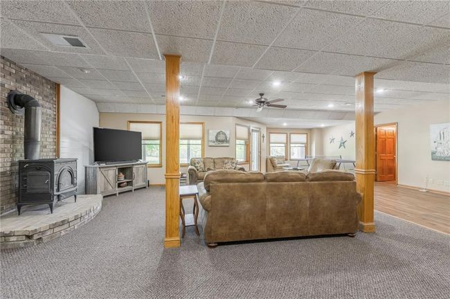 Living area with a wood stove, carpet flooring, visible vents, and a healthy amount of sunlight | Image 60