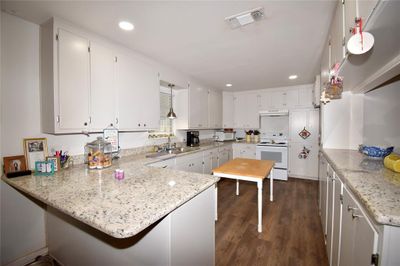 Kitchen featuring dark hardwood / wood-style floors, light stone countertops, white appliances, kitchen peninsula, and white cabinets | Image 3