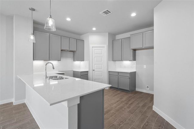 This view of this gorgeous kitchen showcases stained cabinets, quartz countertops, beautiful tile backsplash, high ceiling, recessed and pendant lighting, and tile floors! | Image 5