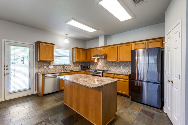 Kitchen with appliances with stainless steel finishes, tasteful backsplash, stone tile floors, and brown cabinets | Image 14