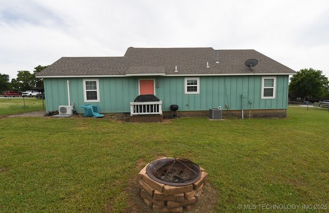 Rear view of property featuring a fire pit, ac unit, board and batten siding, a shingled roof, and central air condition unit | Image 25