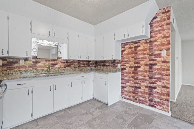 Kitchen featuring a textured ceiling, white cabinetry, decorative backsplash, light stone counters, and white range | Image 8