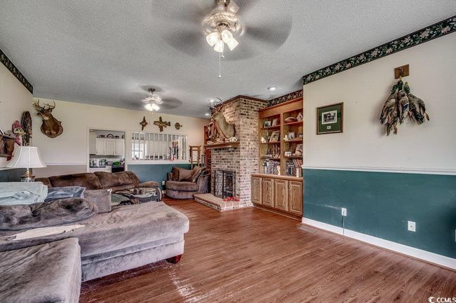 Living area featuring a ceiling fan, a textured ceiling, wood finished floors, a brick fireplace, and baseboards | Image 11