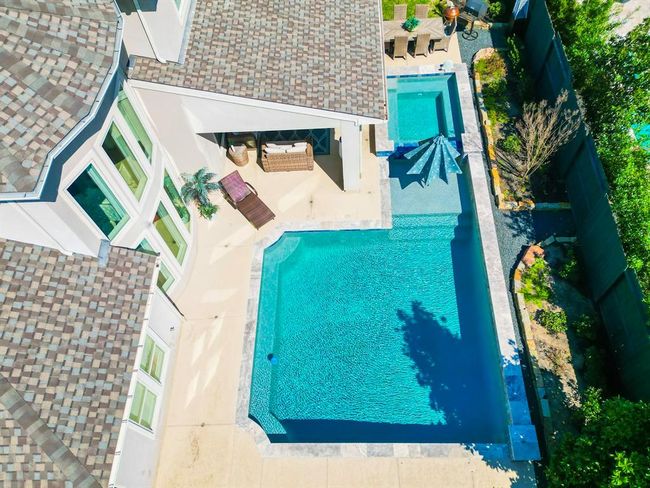 This photo showcases a modern home with a spacious outdoor area featuring a large swimming pool and a connected hot tub. The poolside area includes seating and lush landscaping, perfect for relaxation and entertaining. | Image 47