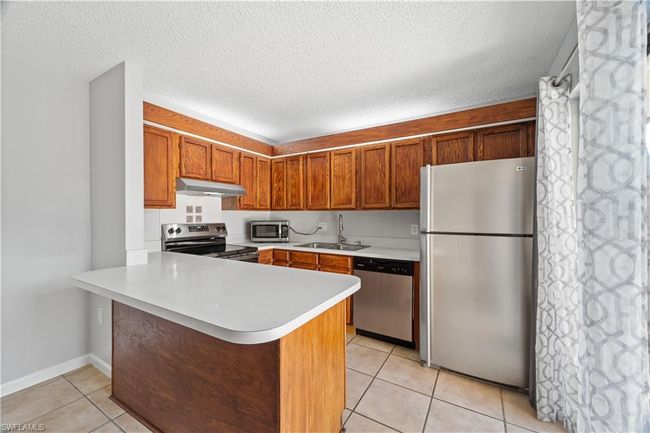 Kitchen featuring a sink, a peninsula, under cabinet range hood, stainless steel appliances, and light tile patterned flooring | Image 6
