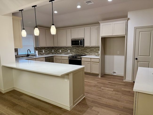 Kitchen featuring appliances with stainless steel finishes, light wood-style flooring, tasteful backsplash, a peninsula, custom cabinets and hanging light fixtures | Image 6