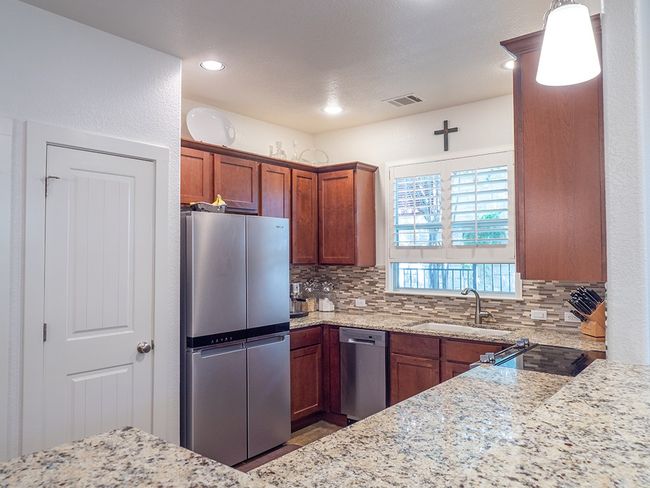 Kitchen with appliances with stainless steel finishes, light stone countertops, decorative backsplash, a textured wall, and recessed lighting | Image 5