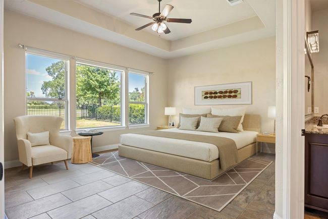 Virtually staged. Primary bedroom with a tray ceiling and a ceiling fan. Also has oversized picture windows with views of the 13th hole fairway. Windows have remote-controlled shades for privacy. | Image 7