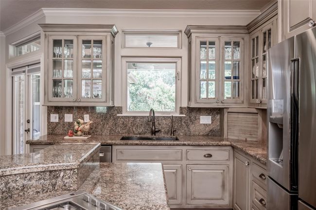 Experience a bright kitchen with glass-front cabinets set against exterior windows, inviting natural light and views of nature. Enjoy watching deer and wildlife beyond the fence. The sink window serves as a convenient passthrough to the “Winter Patio.” | Image 13