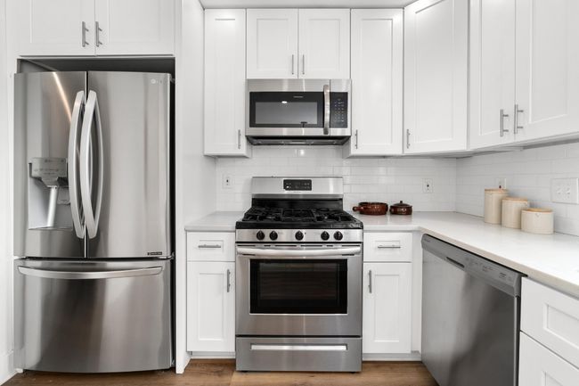 Kitchen featuring stainless steel appliances, white cabinetry, light countertops, and backsplash | Image 9