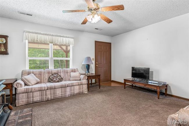 Living room with carpet floors, a textured ceiling, a ceiling fan, and baseboards | Image 14