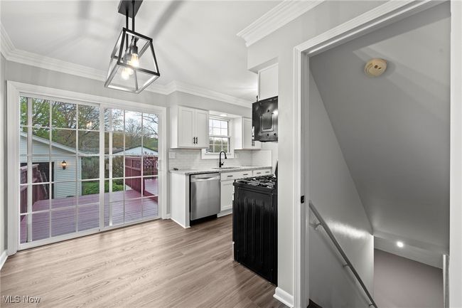 Kitchen featuring white cabinetry, decorative backsplash, stainless steel dishwasher, a sink, and wood finished floors | Image 32